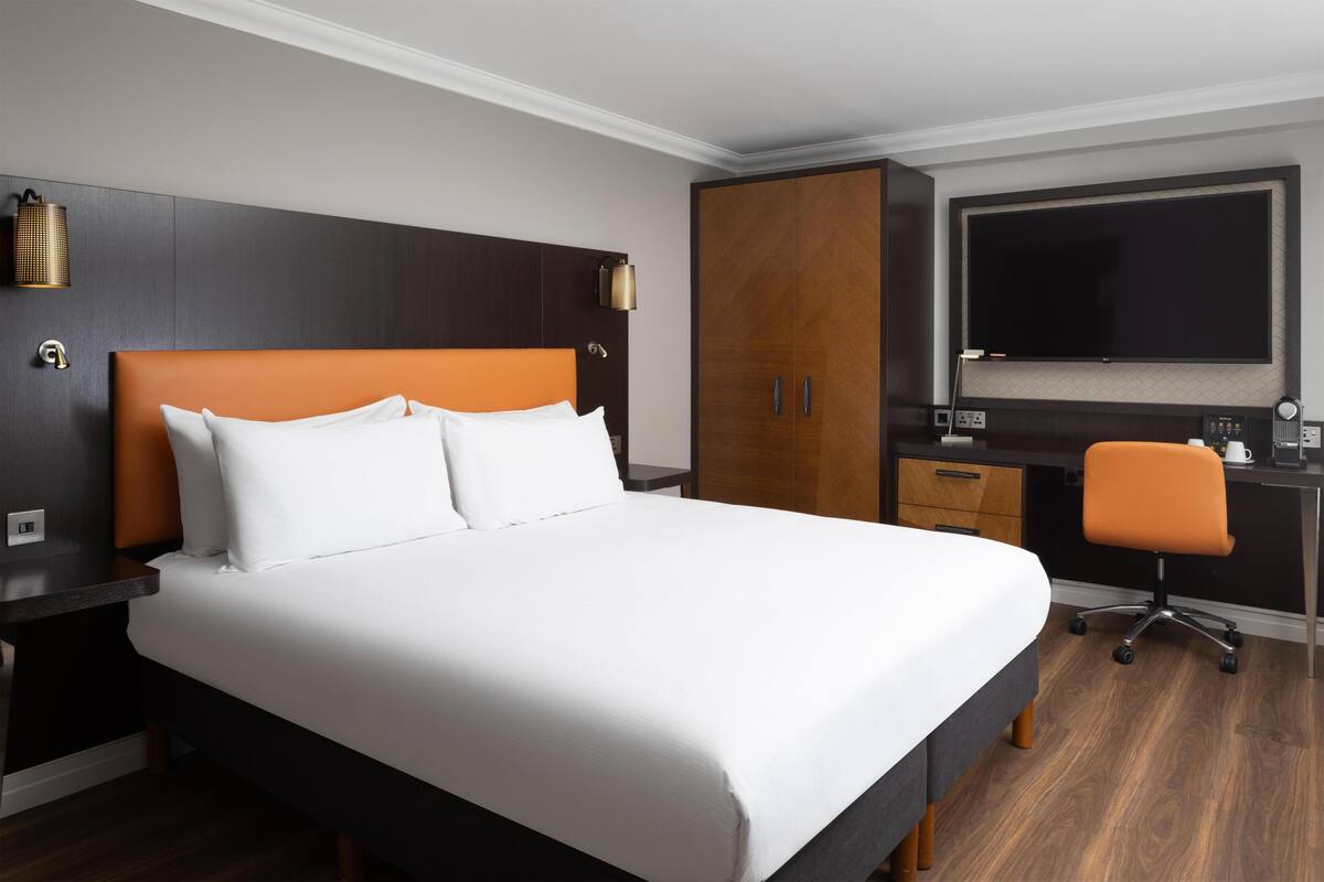 Habitación de hotel con una cama grande, un escritorio con silla, un armario y un televisor de pantalla plana montado en la pared.