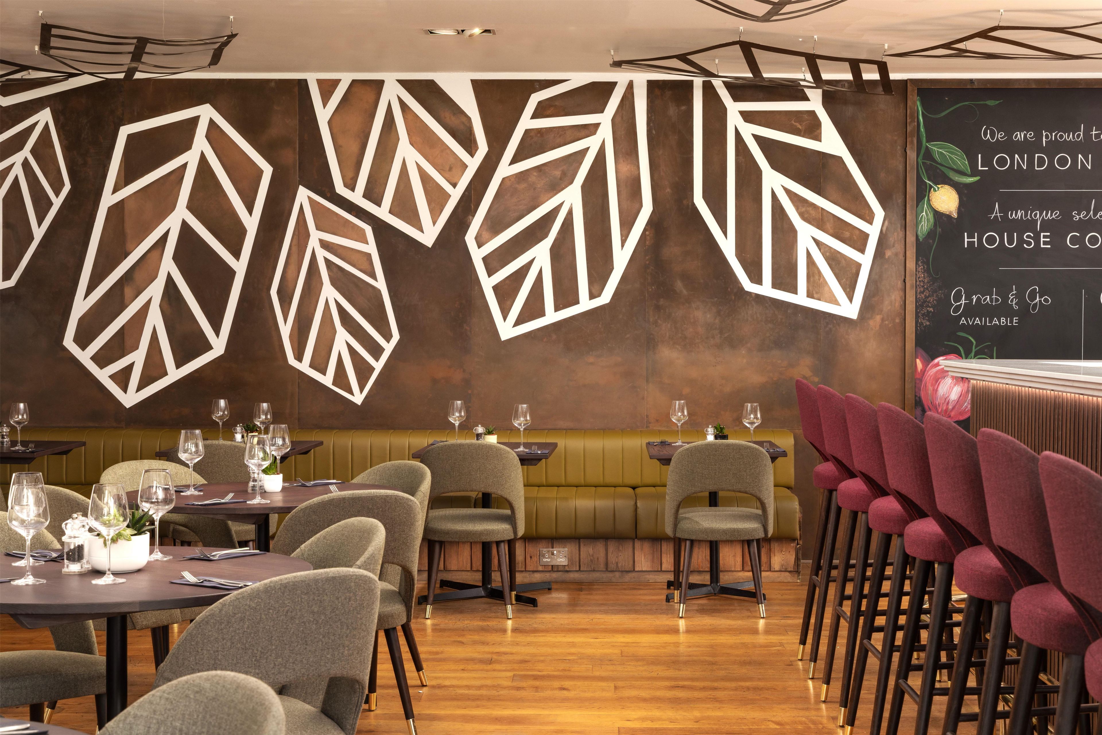 A restaurant interior with a modern design, featuring geometric wall decorations, wooden flooring, and a mix of seating options including booths and high tables.