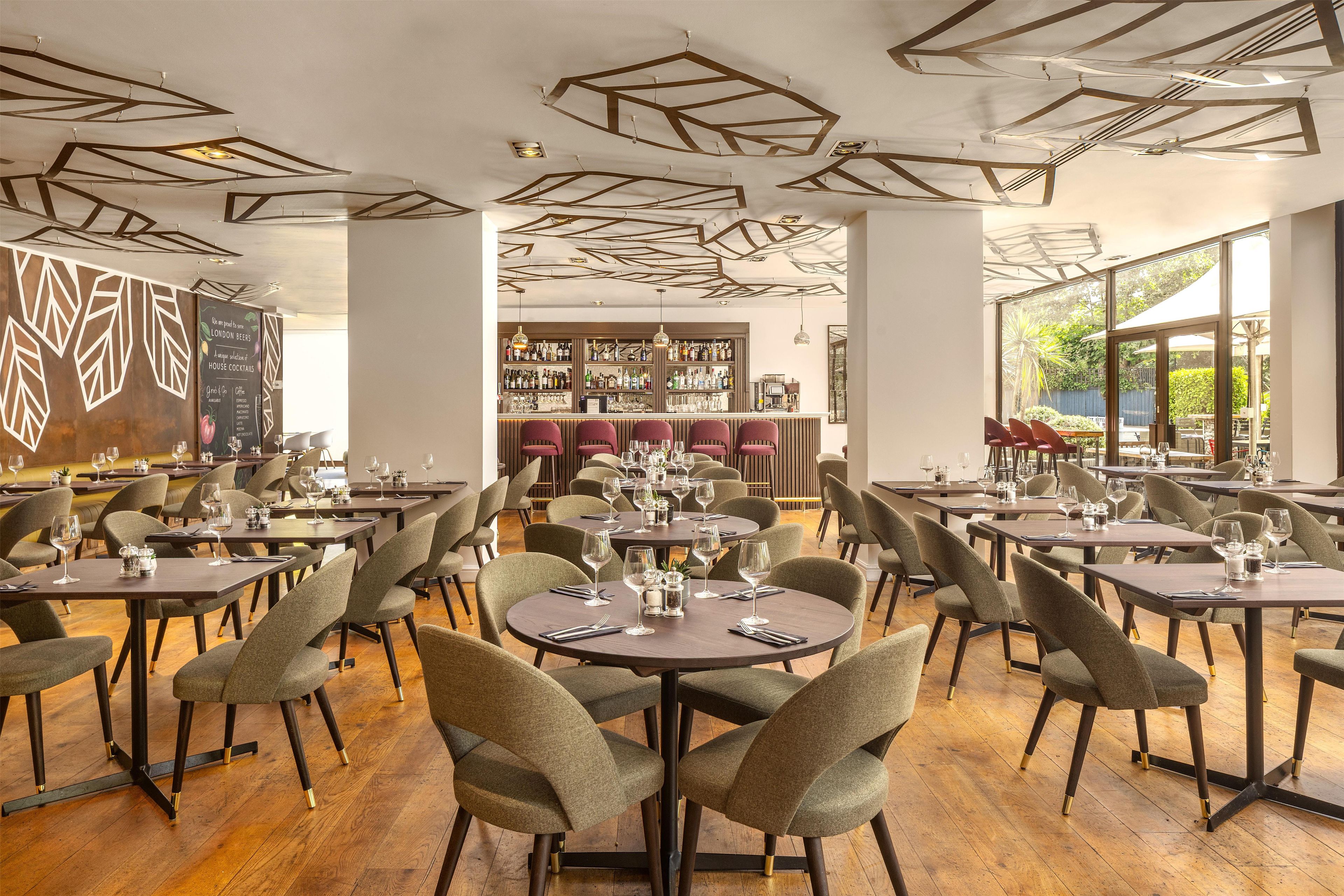 A restaurant with round tables and chairs, a bar area, and a view of the outdoors.