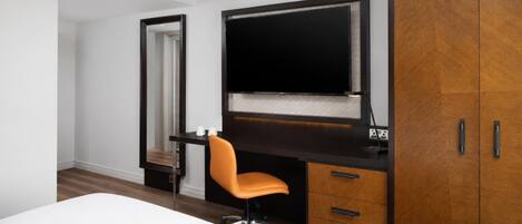 A hotel room with a bed, a desk with a chair, a wardrobe, and a television.