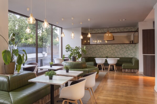 A modern interior with green seating, wooden tables, and hanging pendant lights. - DoubleTree by Hilton Hotel London - Hyde Park (London)