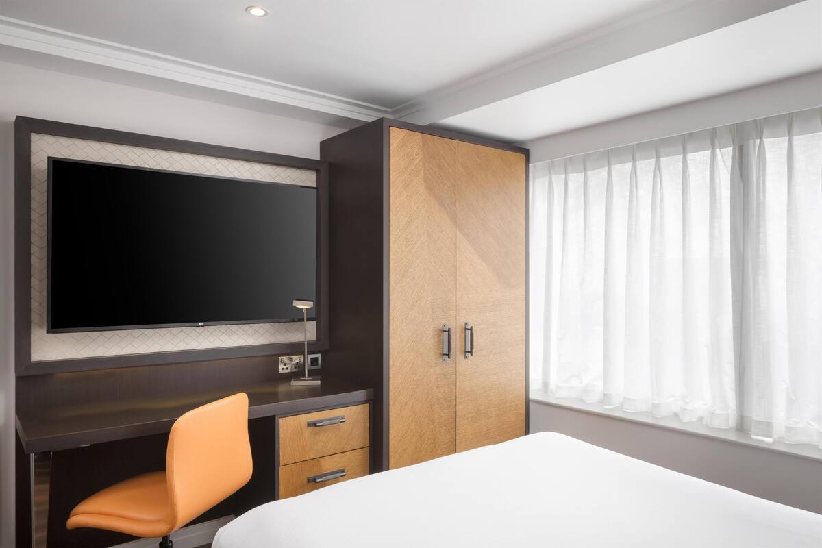 Una habitación de hotel con cama, escritorio con silla, televisor y armario.