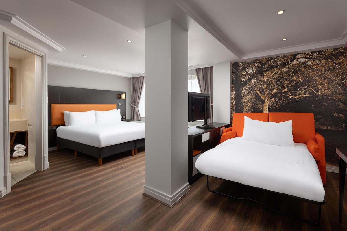 Habitación de hotel con dos camas, un escritorio, una silla y un mural grande con un árbol.