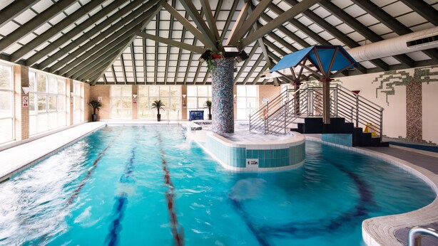 An indoor swimming pool with clear lanes, a central fountain, and a staircase leading to a viewing platform. - Mercure Leeds Parkway Hotel (Leeds)