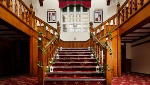 A grand staircase with ornate wooden railings and red carpeted steps, leading to a landing with a white door and framed pictures above. - Mercure Leeds Parkway Hotel (Leeds)