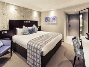 Une chambre d’hôtel avec un lit, un bureau, une chaise et une porte de salle de bain.