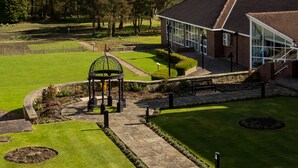 A building with a glass facade, surrounded by a well-maintained lawn and a garden area with a gazebo. - Mercure Leeds Parkway Hotel (Leeds)