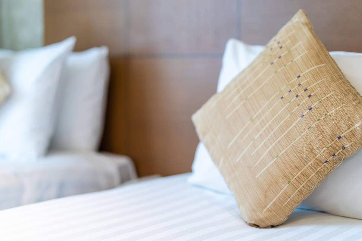 A neatly made bed with white bedding and a single decorative pillow with a woven texture.