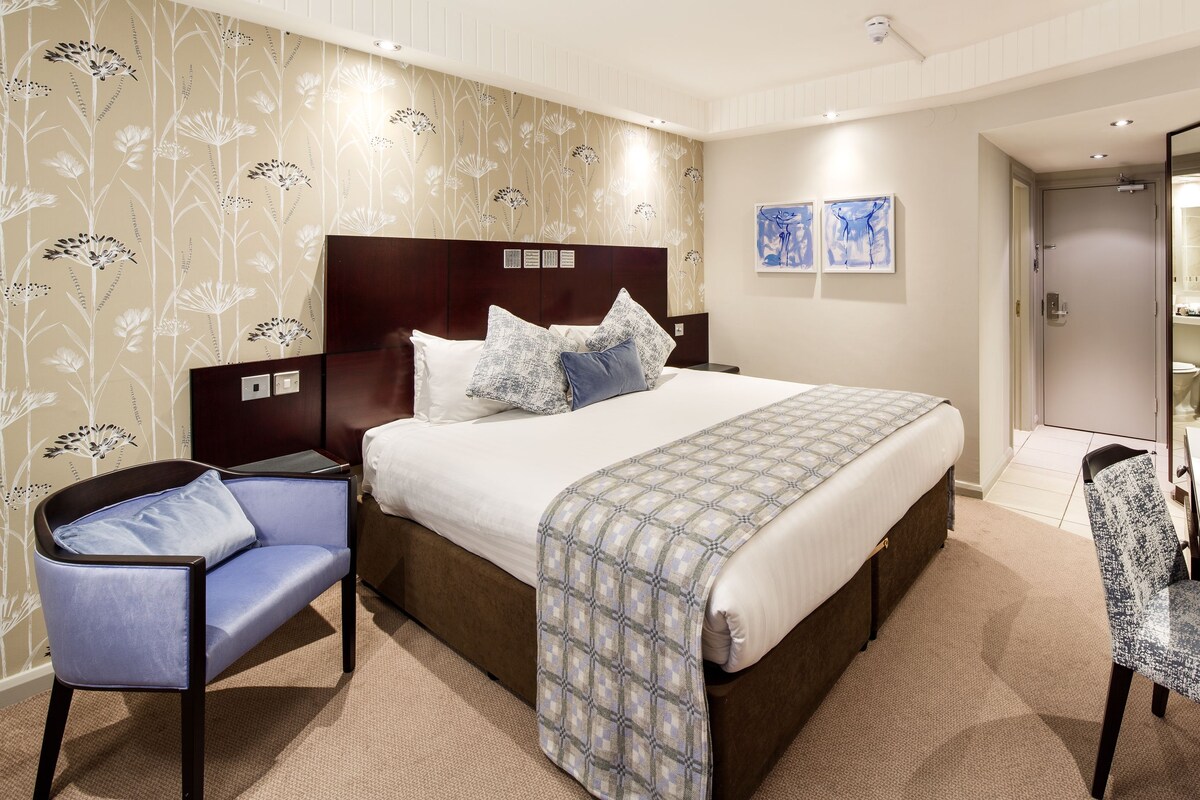 A hotel room with a bed, a desk, a chair, a television, and artwork on the wall.