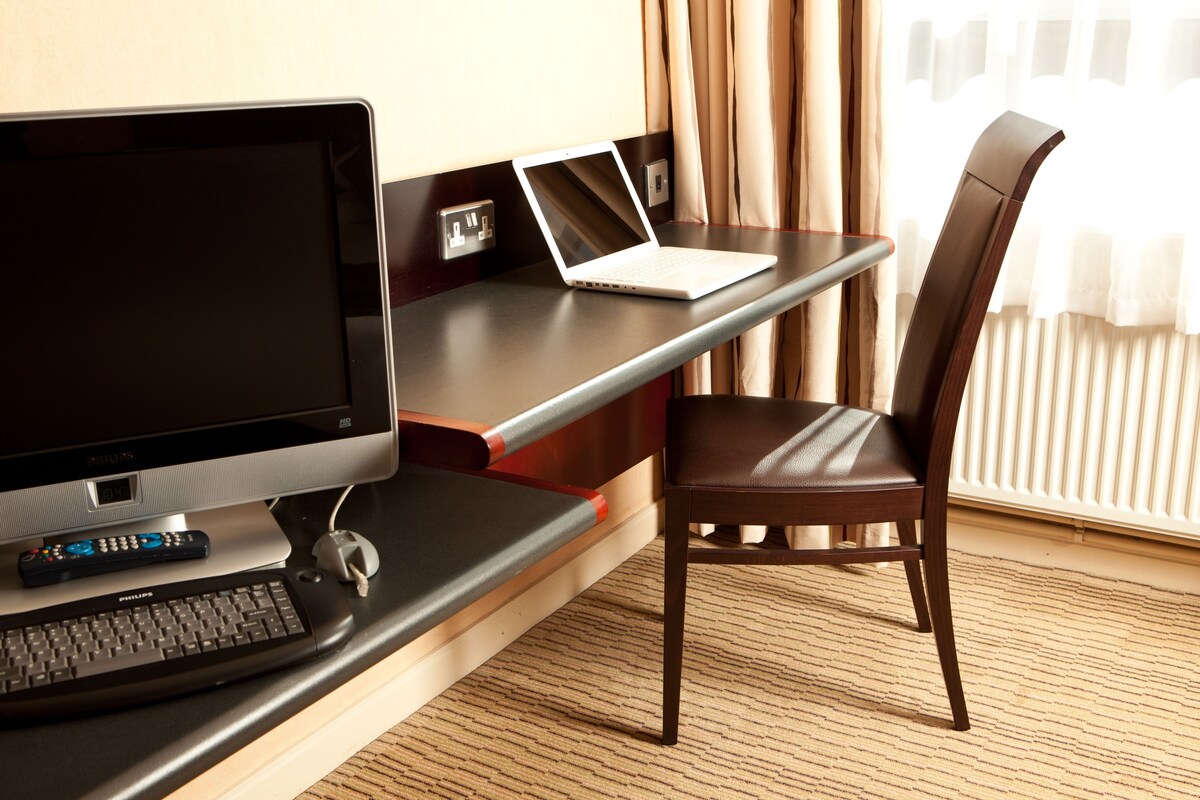 A hotel room with a desk, a laptop, a television, and a chair.
