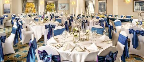 A banquet hall with round tables set for a formal event, featuring white tablecloths and blue sashes on chairs.