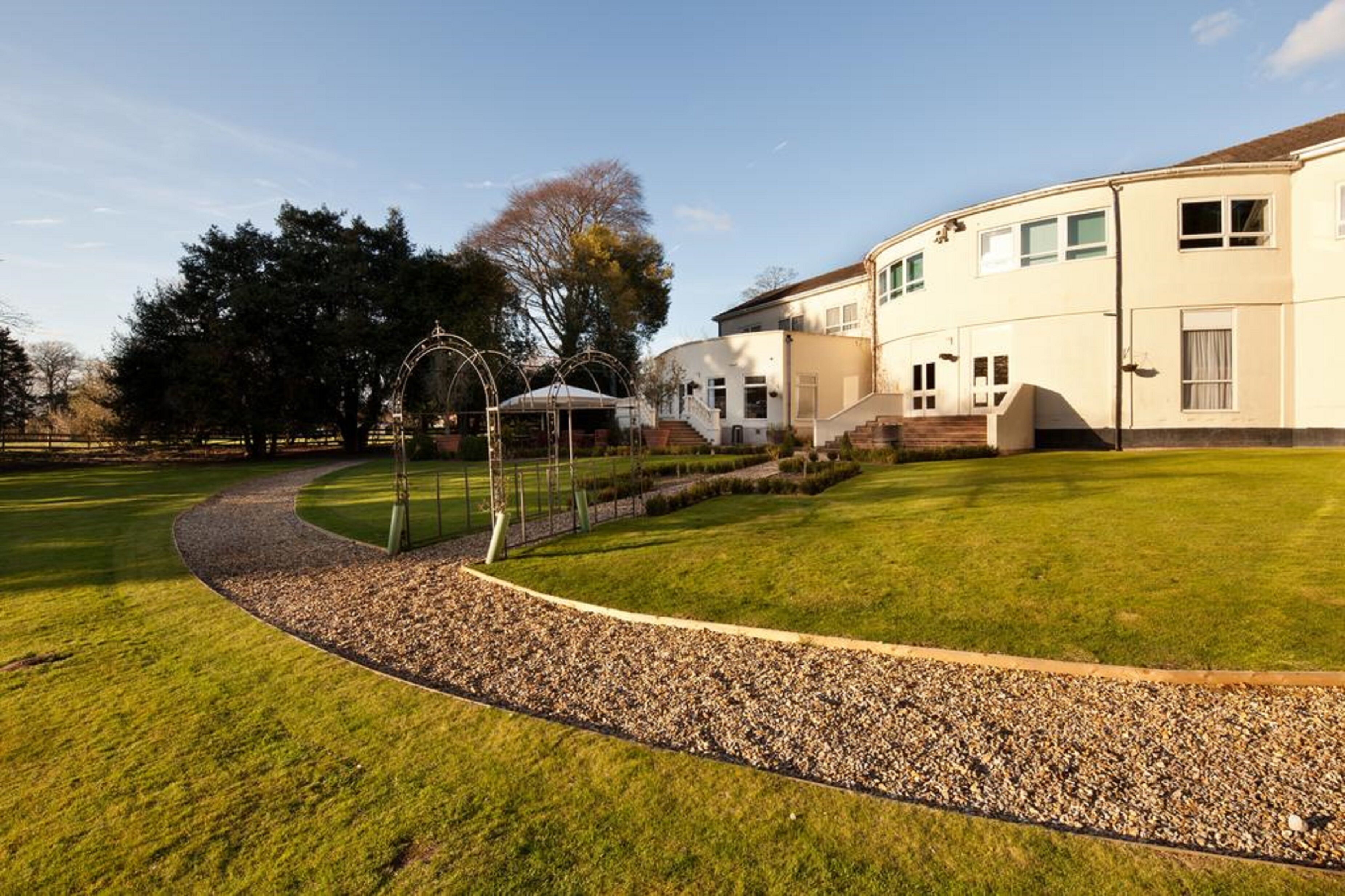 A well-maintained lawn with a gravel path leading to a building with multiple windows and a covered outdoor area.