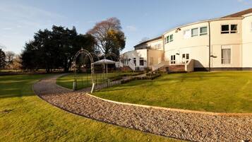 A well-maintained lawn with a gravel path leading to a building with multiple windows and a covered outdoor area.