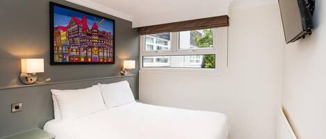 A hotel room with a large bed, bedside lamps, a painting on the wall, a window with a view, and a flat-screen TV mounted on the wall.