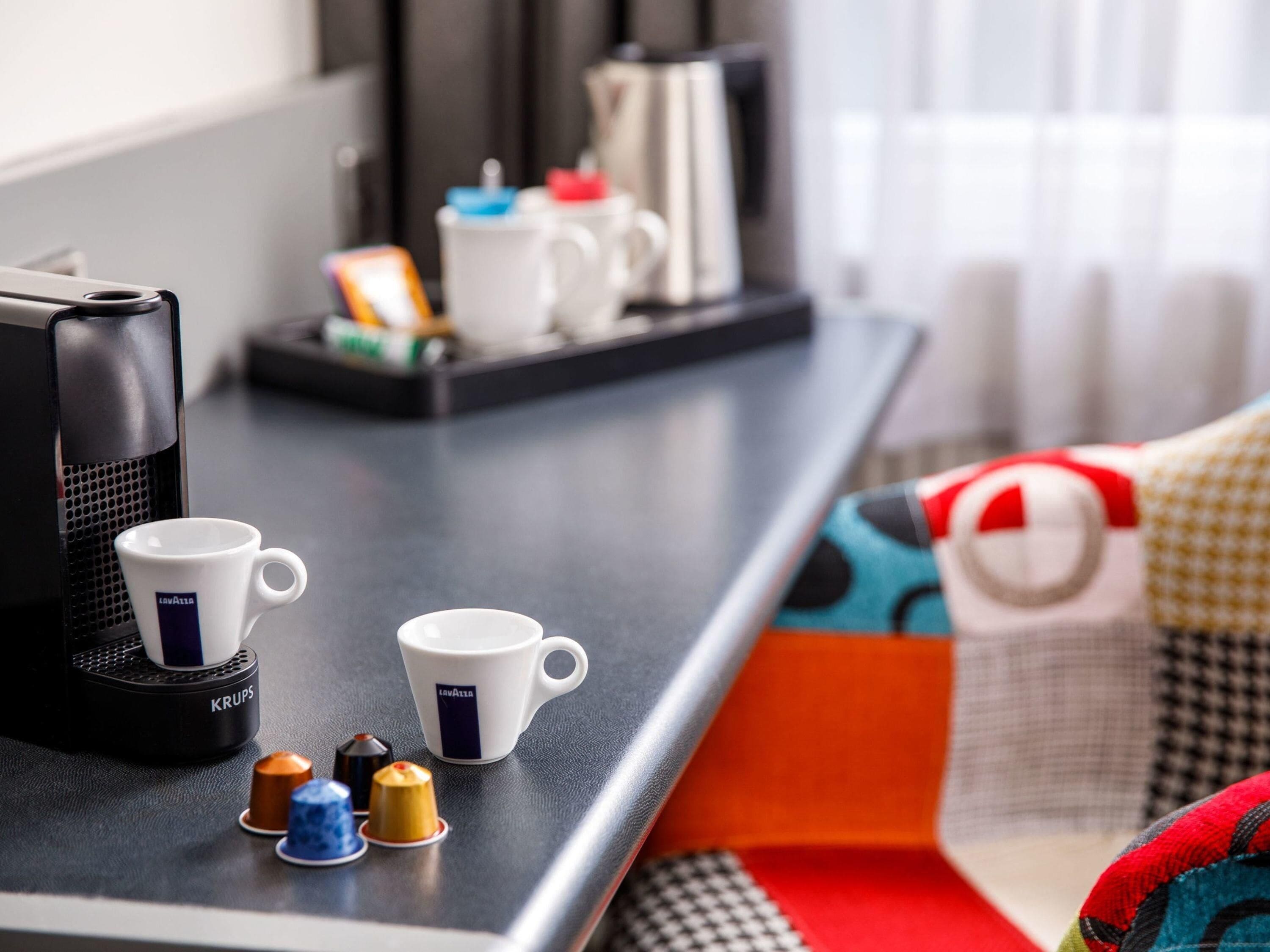 A coffee machine, two white cups, and a tray with a kettle and other items on a table.