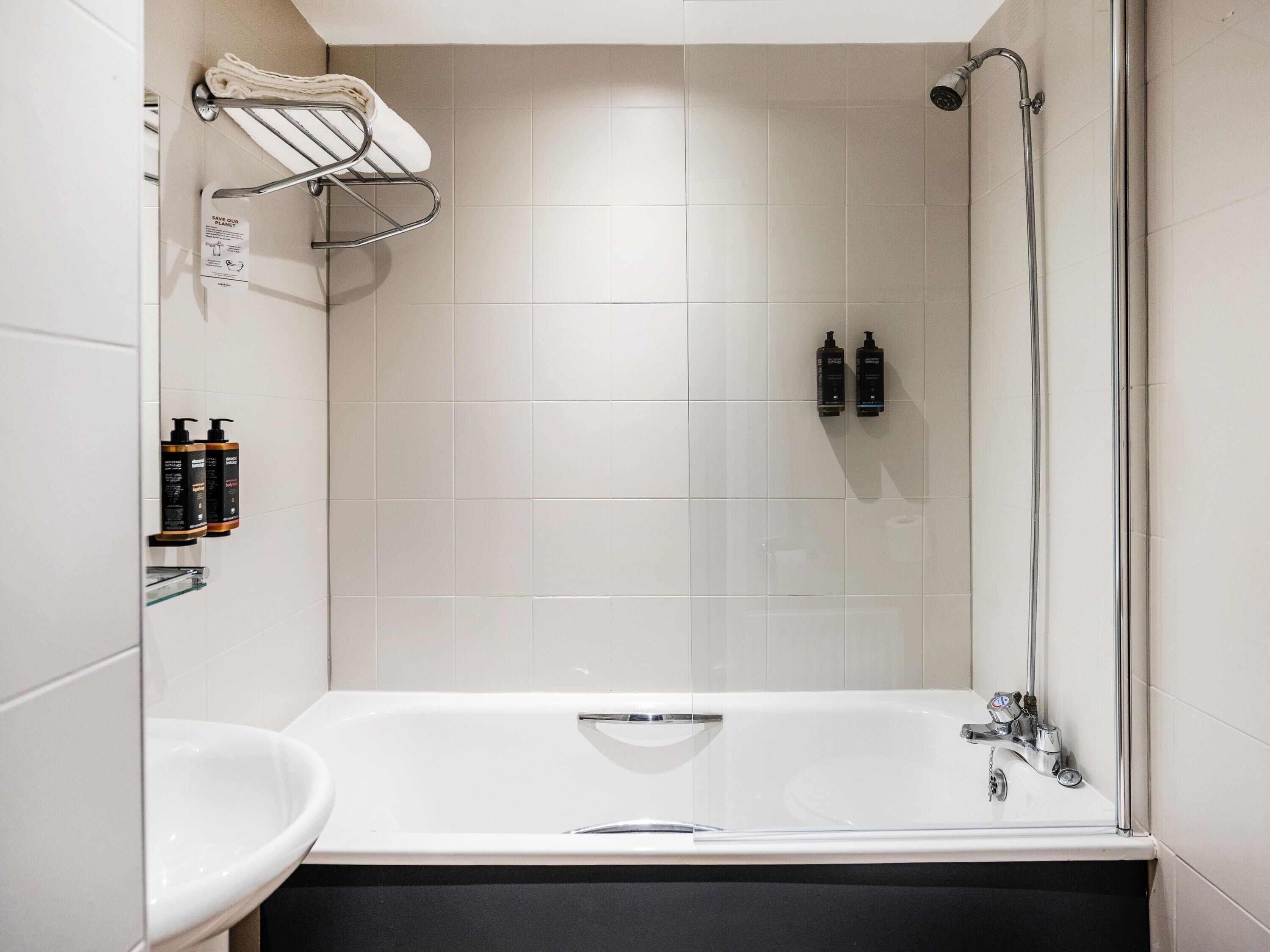 A modern bathroom with a bathtub, a shower, and a toilet. There are two bottles of shampoo and conditioner on the wall.