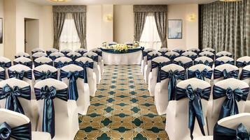 A room with rows of chairs with white covers and dark sashes, a patterned carpet, and a table with a floral arrangement.