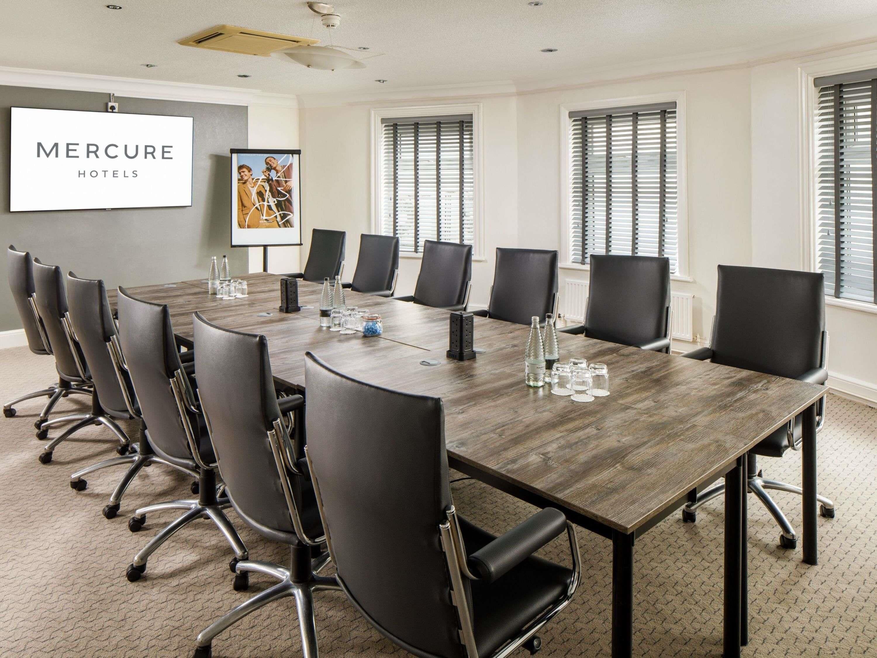 A conference room with a long table, black chairs, and a 'Mercure Hotels' sign.
