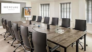A conference room with a long table, black chairs, and a 'Mercure Hotels' sign.