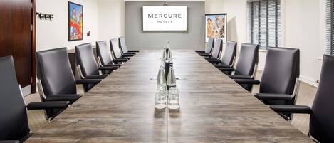 A conference room with a long table, black chairs, and a projector screen displaying 'Mercure Hotels'.