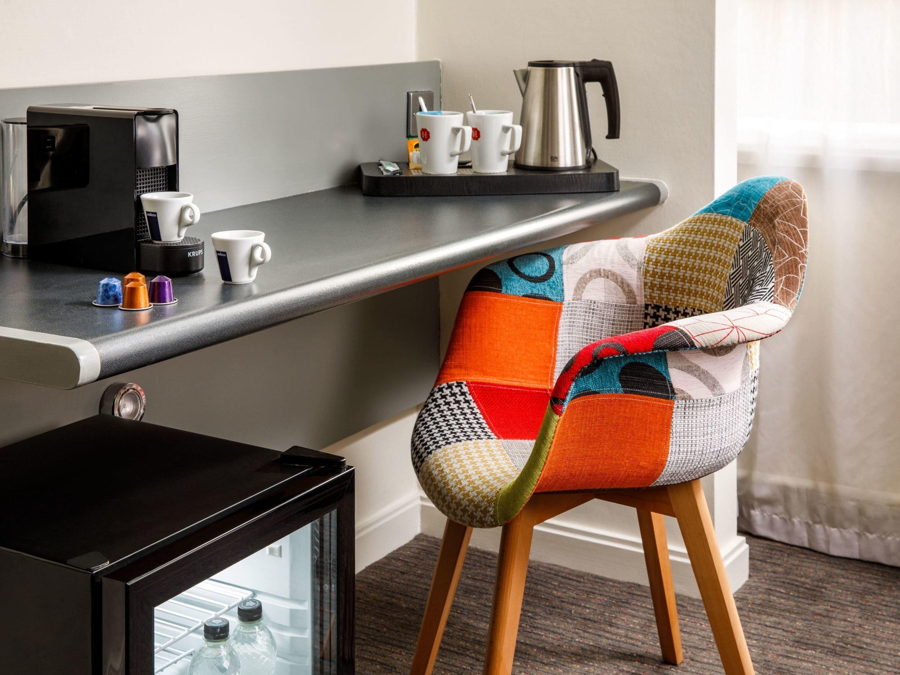 A modern kitchen area with a coffee machine, a kettle, and a glass cabinet.