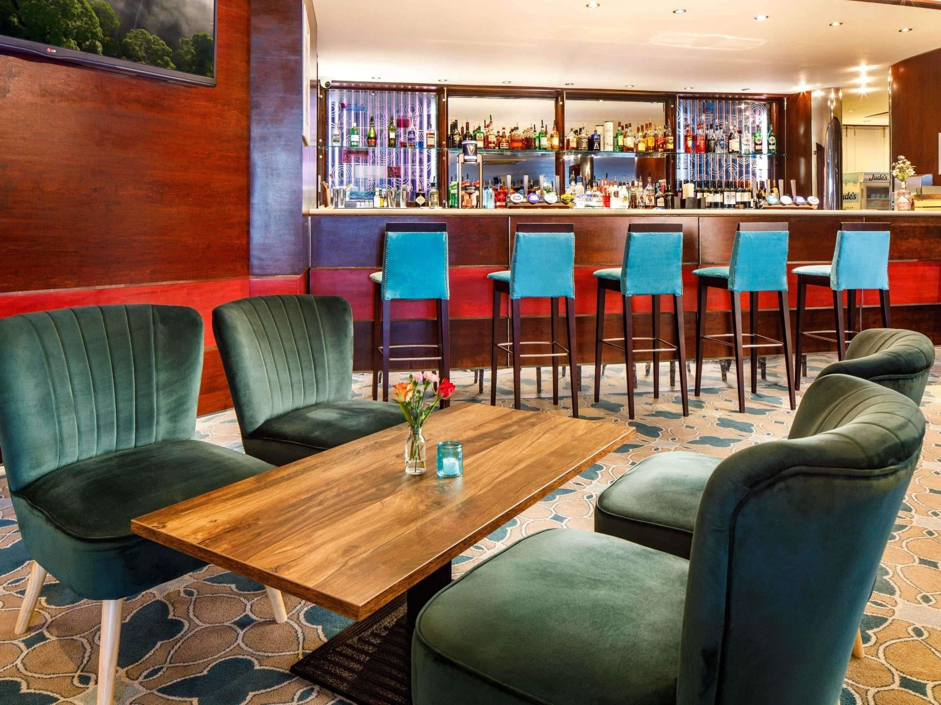 A bar area with multiple seating options, a wooden table, and a variety of bottles on shelves.