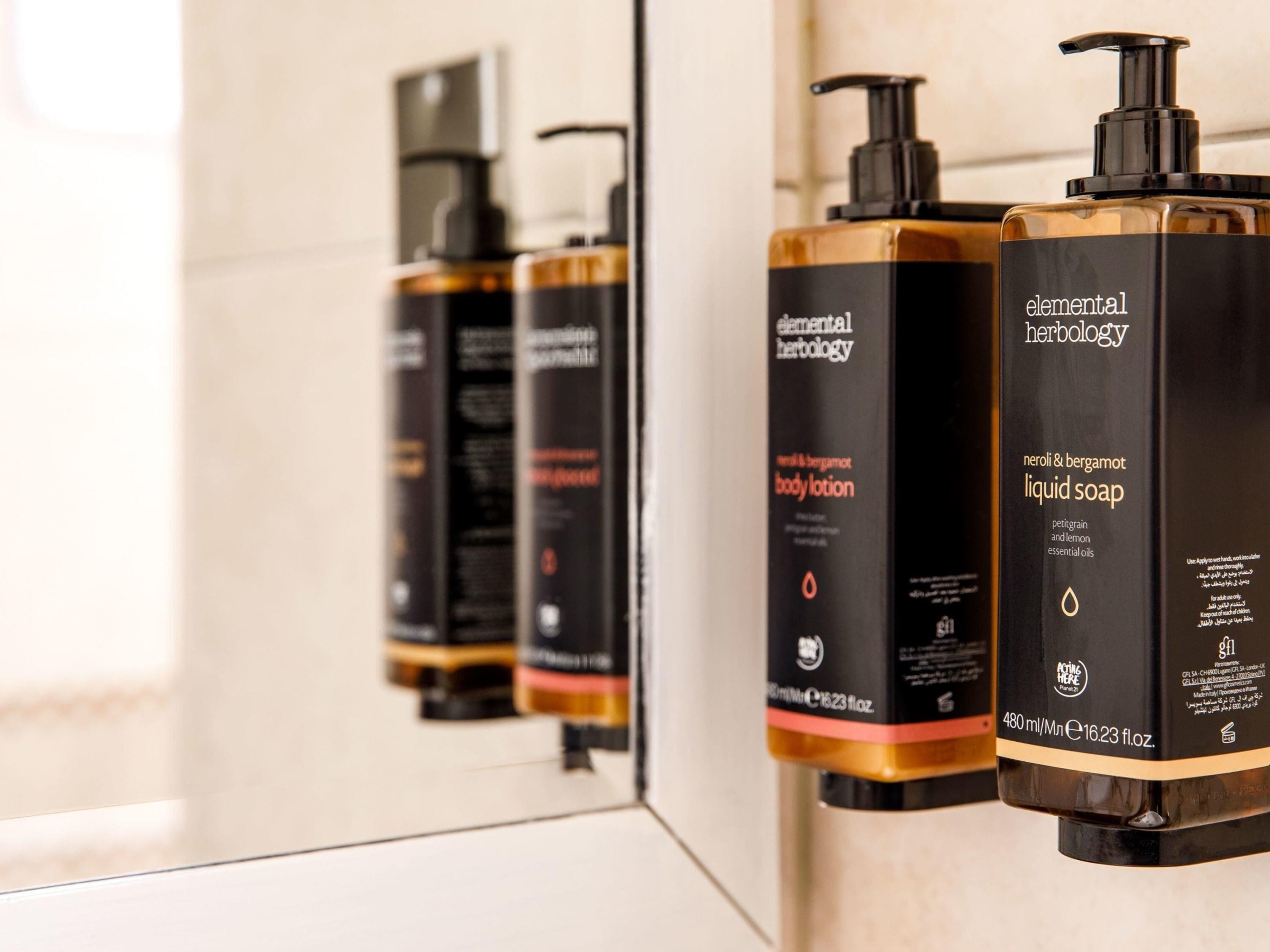 Three bottles of Elemental Herbology body lotion, liquid soap, and body oil on a bathroom counter.