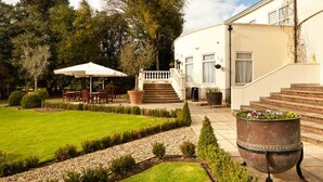 A well-maintained garden with a patio area, outdoor seating, and a large decorative pot. - Mercure Chester Abbots Well Hotel (Chester)