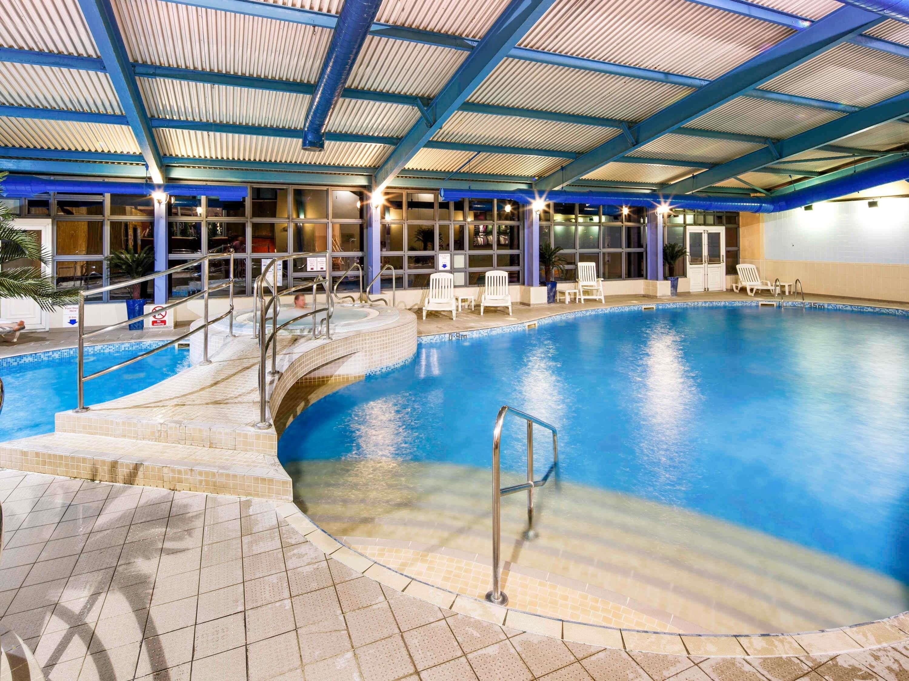 An indoor swimming pool with a covered roof, clear water, and steps leading into the pool.