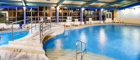 Una piscina interior con techo cubierto, agua cristalina y escalones de acceso.