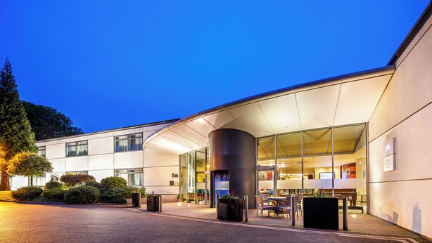 A modern hotel with a curved entrance, large windows, and outdoor seating. - Mercure Chester Abbots Well Hotel (Chester)