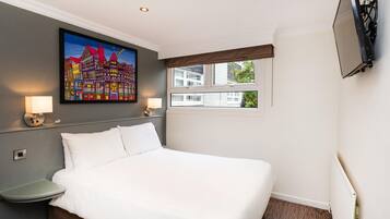 Una habitación de hotel con una cama, lámparas de noche, un cuadro, una ventana y un televisor montado en la pared.