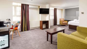 Camera d'albergo con scrivania, sedia, divano, televisore, letto e un minibar.