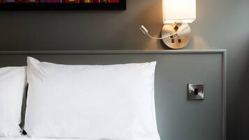 Ein ordentlich bezogenes Bett mit weißen Leinen, eine wandmontierte Lampe und eine kleine Steckdose.