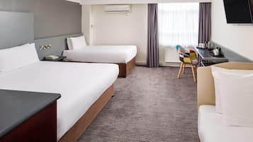 A hotel room with two beds, a desk, a chair, a TV, and a window with curtains.