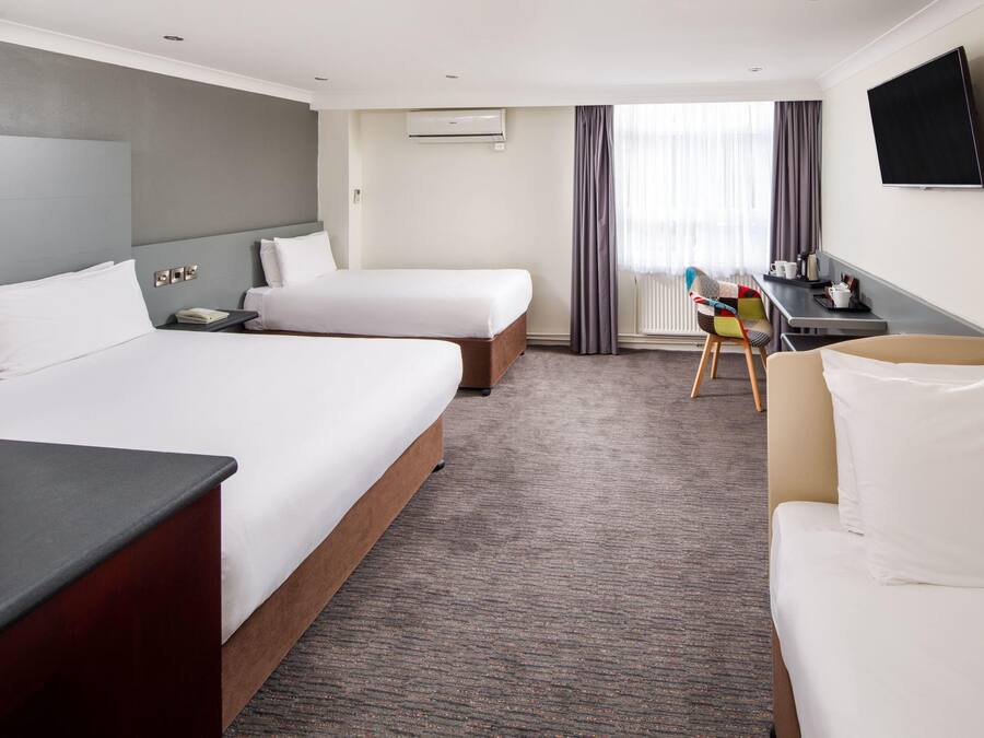A hotel room with two beds, a desk, a chair, a TV, and a window with curtains.