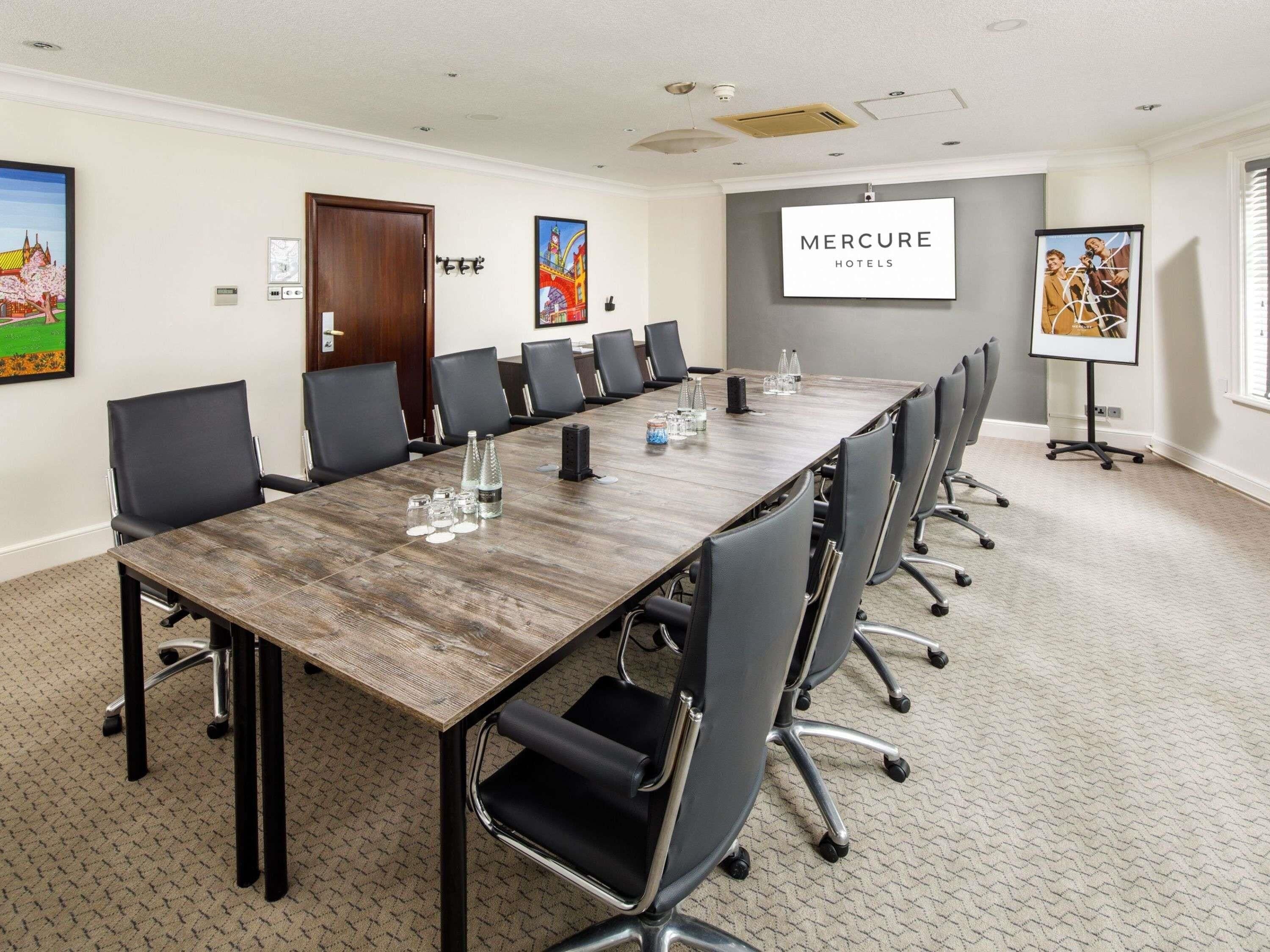 Une salle de conférence avec une longue table, des chaises noires et un panneau « MERCURE HOTELS » sur le mur.
