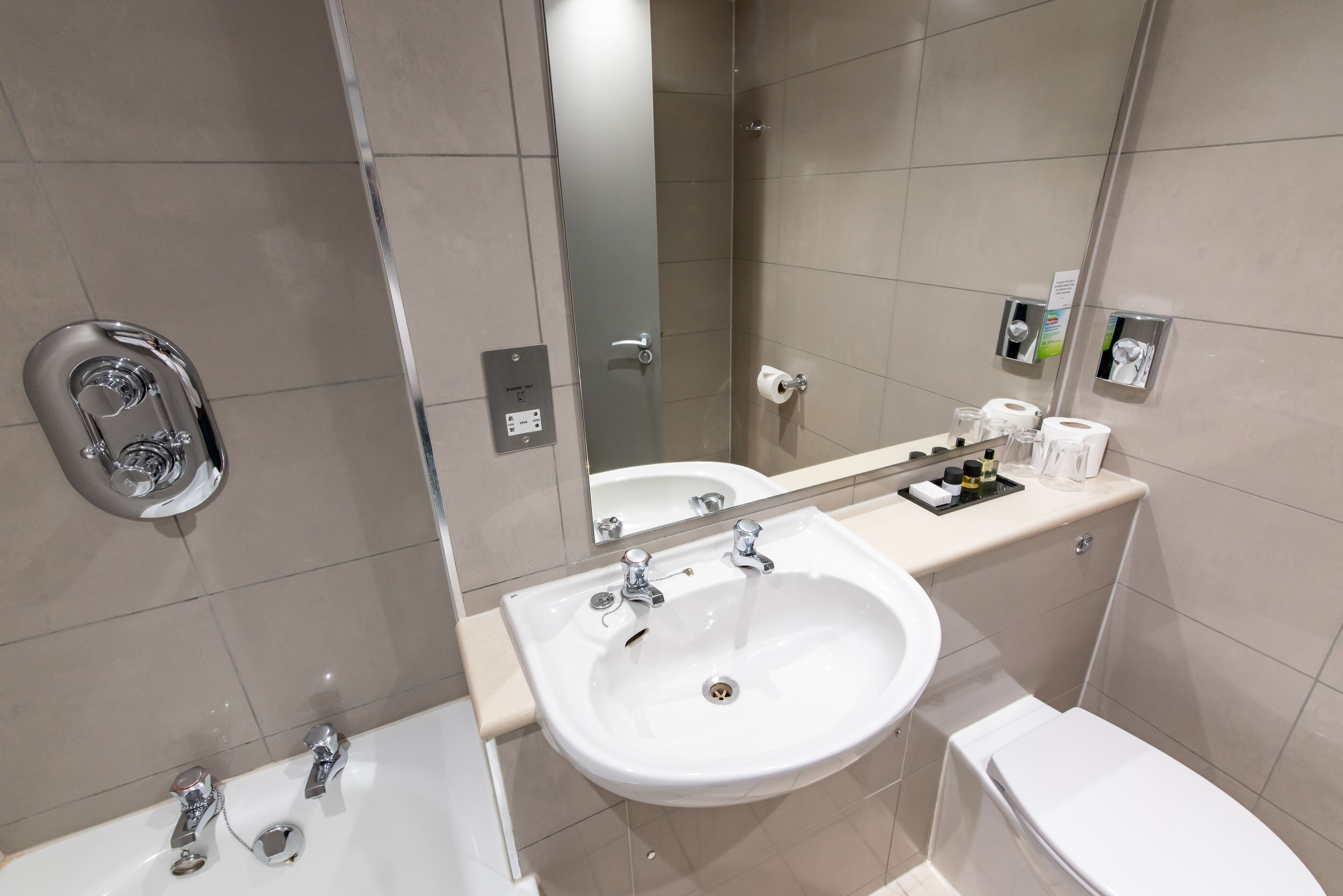 A modern bathroom with a white sink, two faucets, a toilet, and a shower.