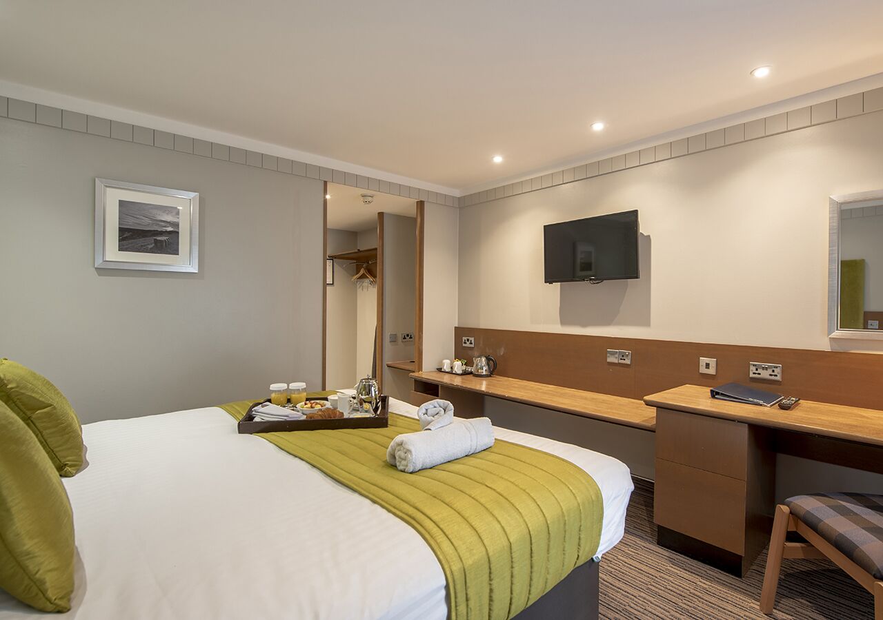Et hotelværelse med seng, skrivebord, spejl og fjernsyn.