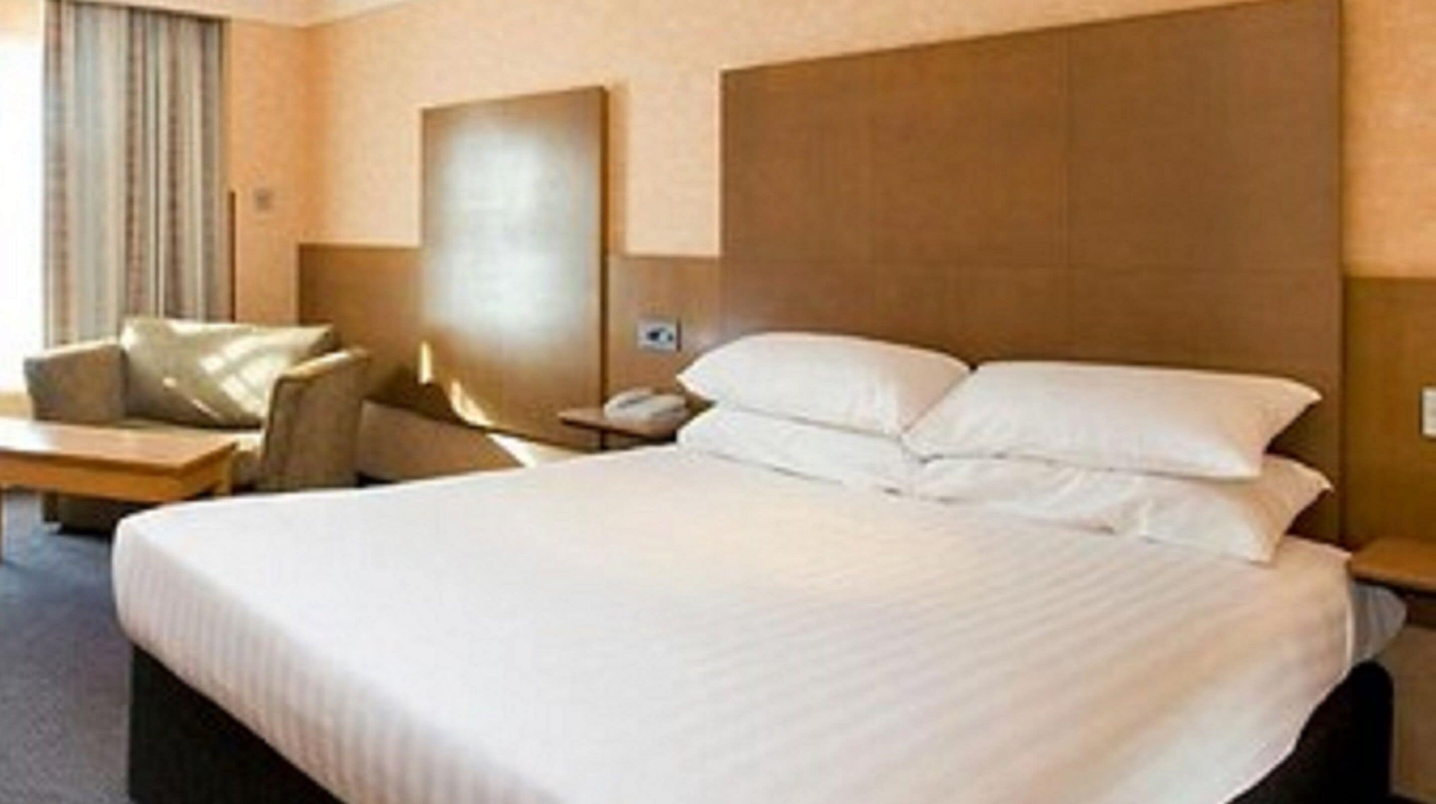A hotel room with a large bed, a bedside table, a chair, and a headboard.