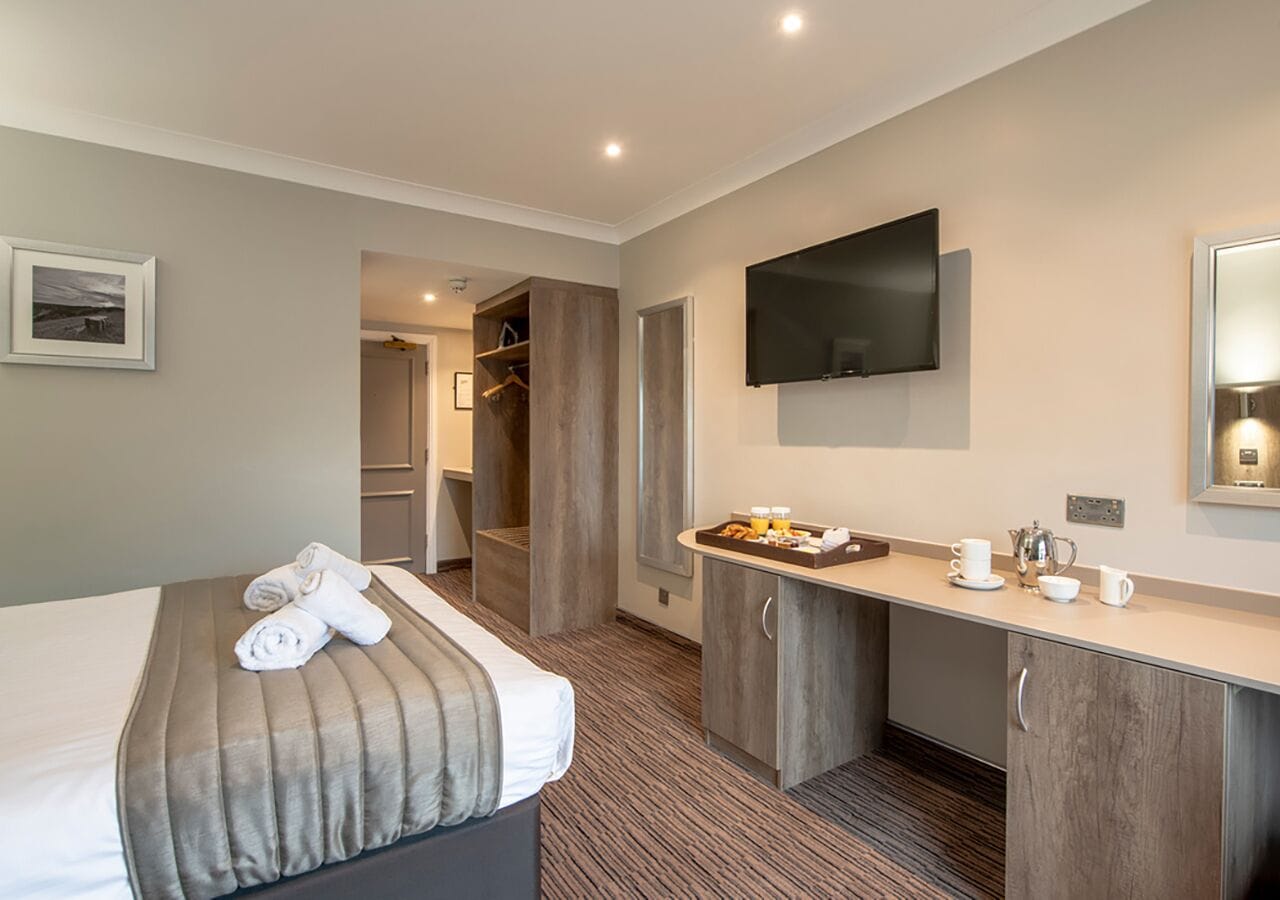 Habitación de hotel con cama, escritorio, televisor de pantalla plana y baño visible a través de una puerta abierta.