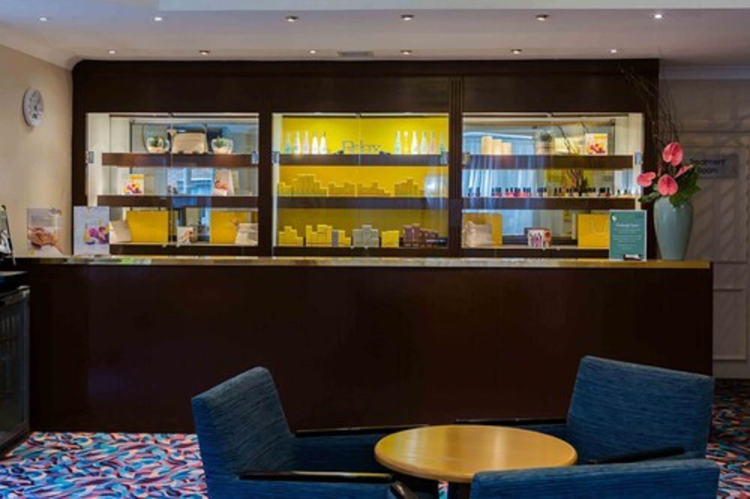 A reception area with a counter displaying various items, two blue chairs, and a small round table.