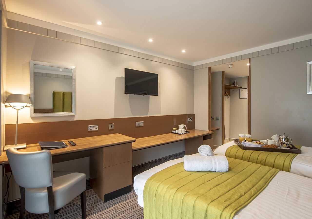 A hotel room with a desk, chair, bed, and a television mounted on the wall.