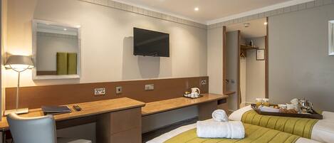 A hotel room with a desk, chair, bed, and a television mounted on the wall.