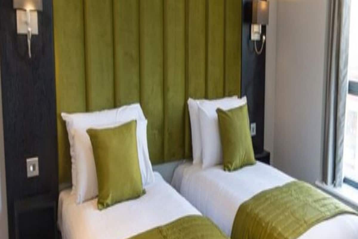 Een hotelkamer met twee bedden, elk met een groene hoofdbord en passende groene sierkussens.