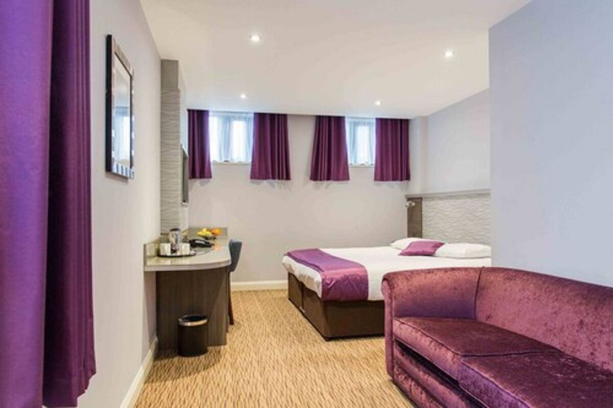 Een hotelkamer met een bed, een bureau, een paarse bank en een kleine prullenbak.