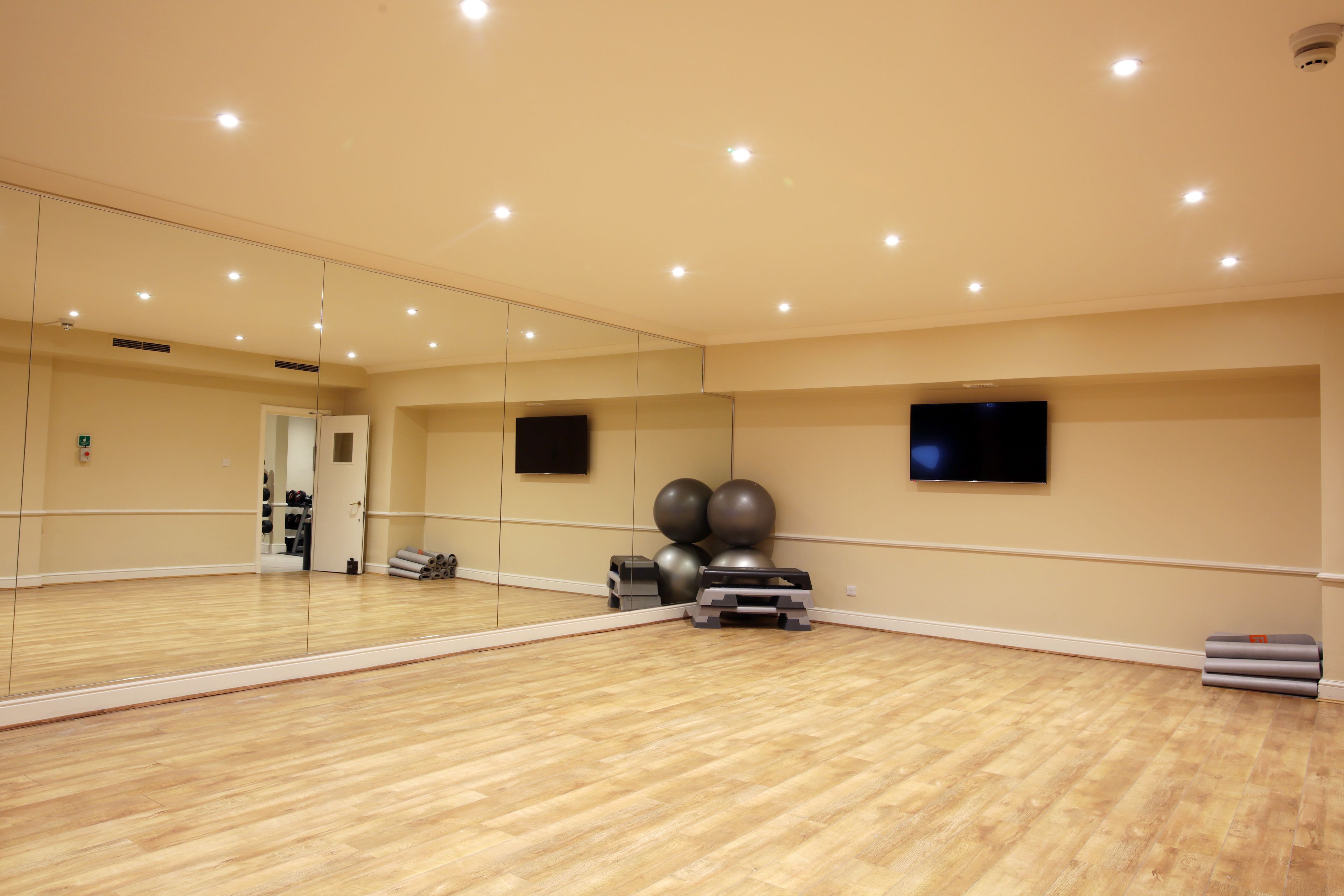 A spacious room with a large mirror, wooden flooring, exercise balls, and a TV mounted on the wall.