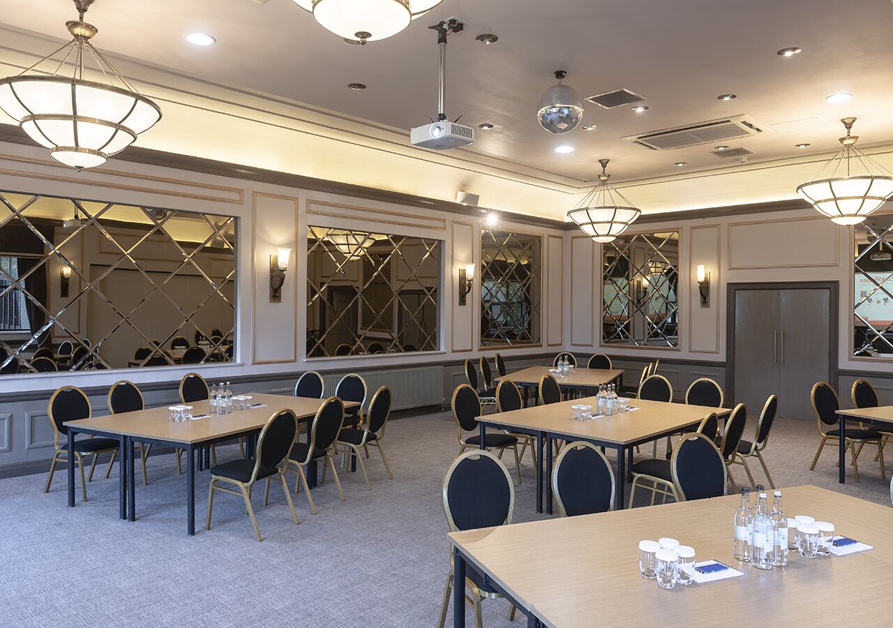 A conference room with multiple tables and chairs, equipped with projectors and lighting fixtures.