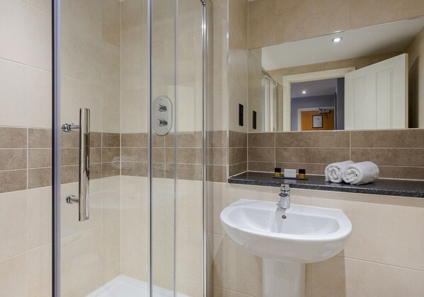 A modern bathroom with a glass-enclosed shower, a white sink, and a countertop with toiletries. - The Hog's Back Hotel & Spa Farnham (Farnham)