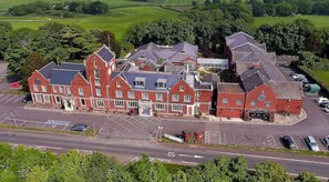 Traditional building with a central entrance and available parking, set amidst green fields and trees.